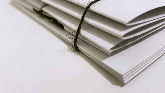 A stack of folded white papers bound together with a piece of twine, shown in close-up on a plain surface.